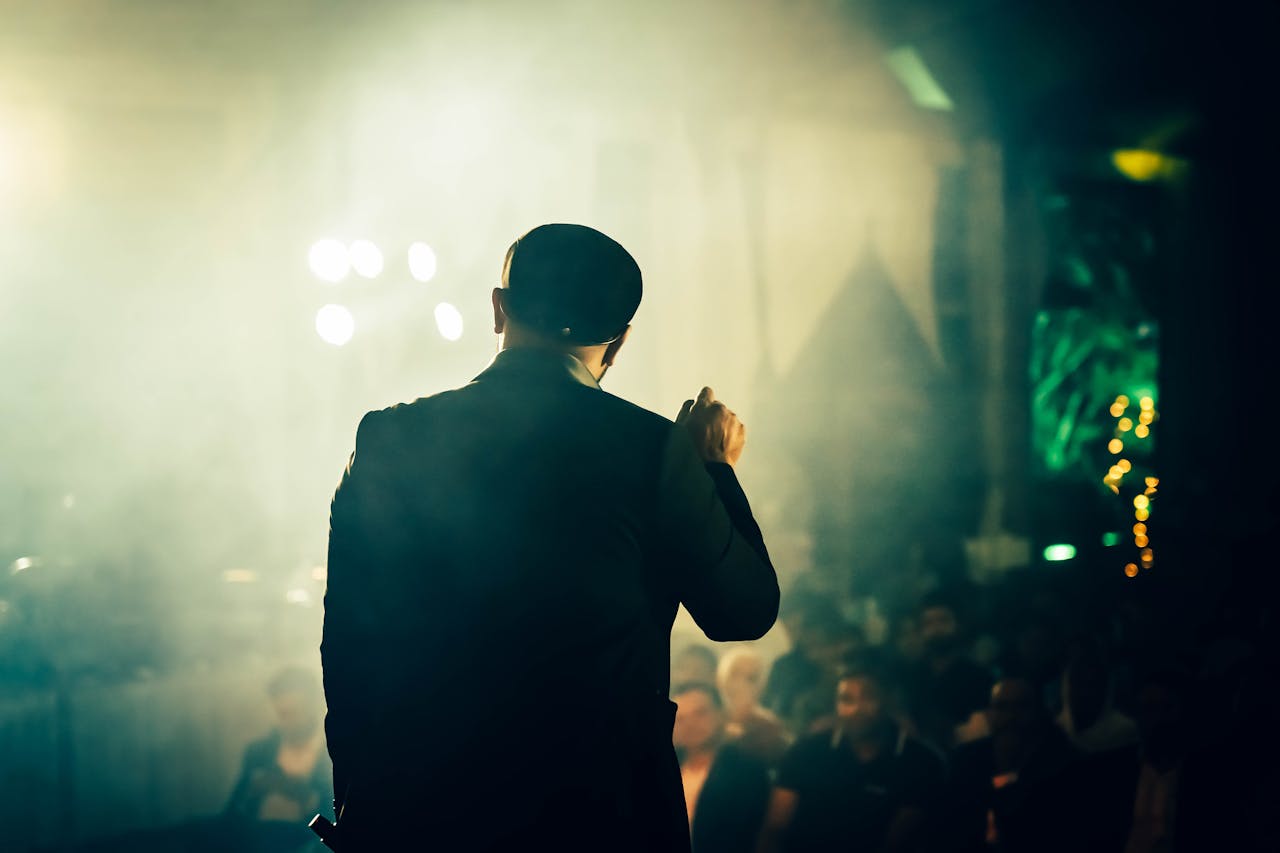 A man seen from the back speaking to an audience at an atmospheric entertainment venue.