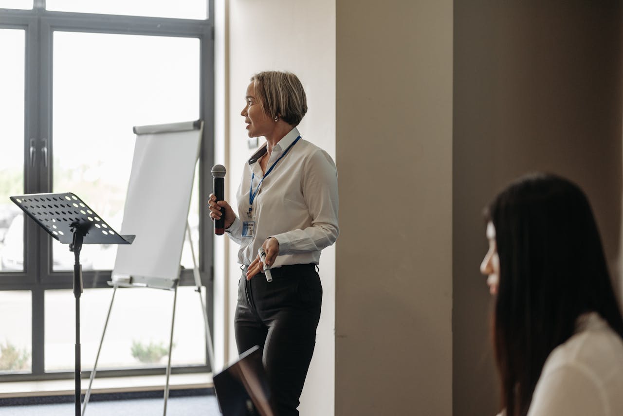 A woman presenting with microphone and flipchart in a conference room.