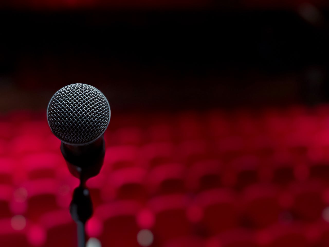 Close-up of microphone on stage with empty red seats in background.